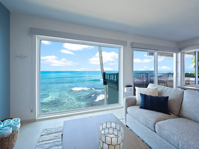 Living room window framing ocean waves and lanai